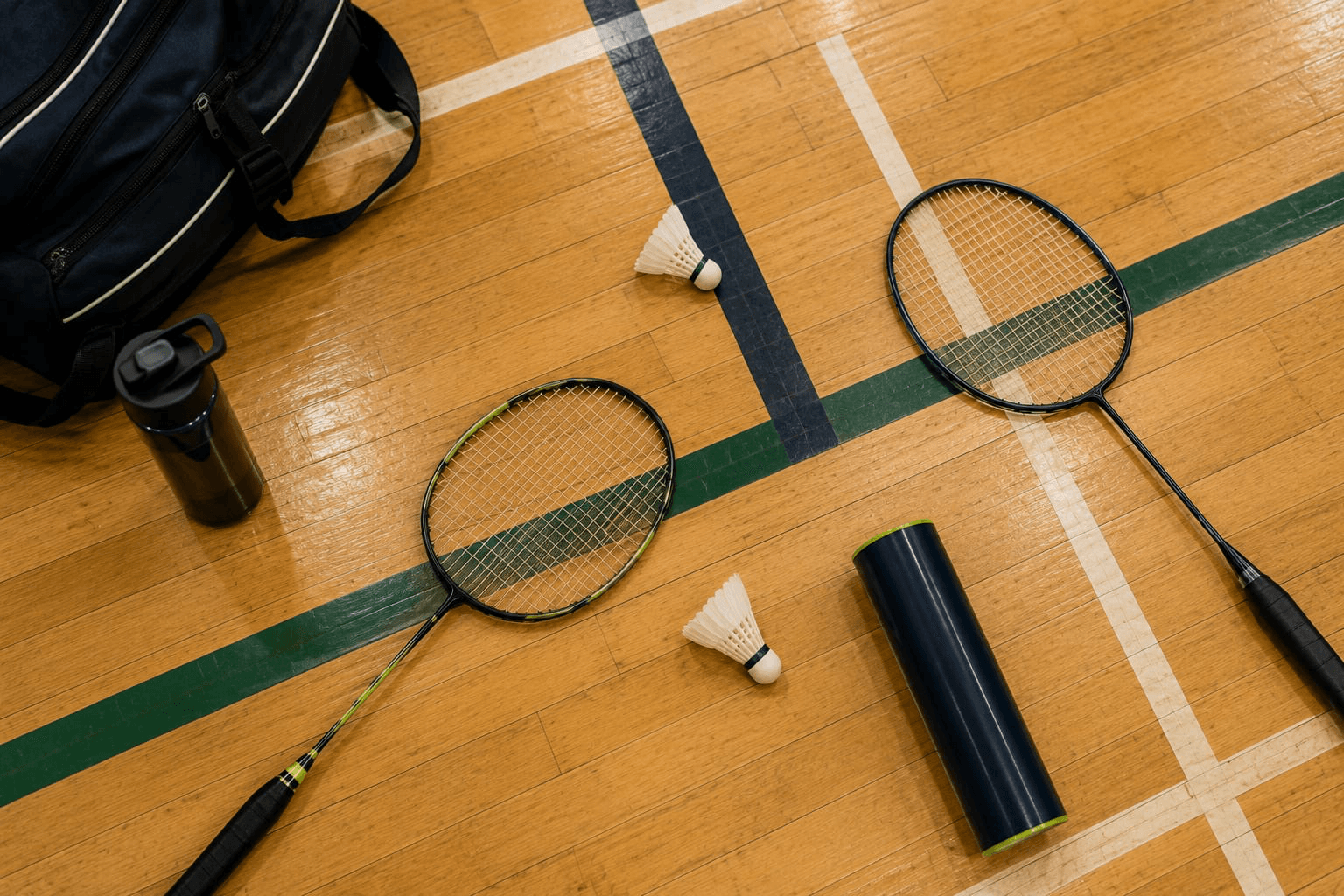 Badminton racquets, shuttlecocks, water bottles, and a kit bag arranged on a gym floor